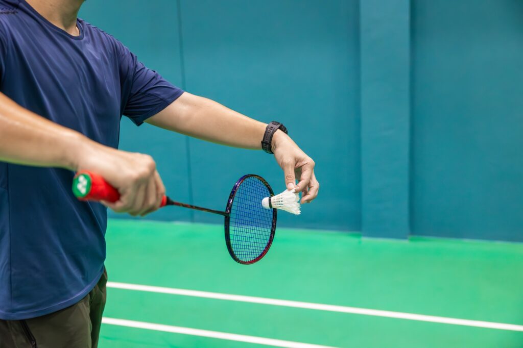 Badminton player hand serving holding shuttlecock and professional badminton racket at indoor sport