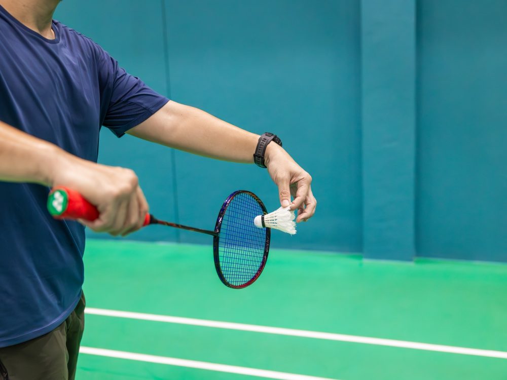 Badminton player hand serving holding shuttlecock and professional badminton racket at indoor sport