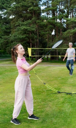 Focus on young woman with racket playing badminton with man in the park. Friends having fun