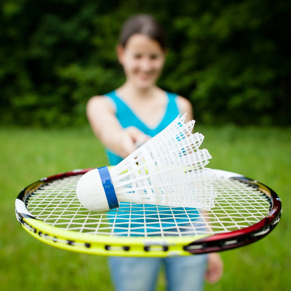 Pretty, young woman playing badminton in a city park on a lovely