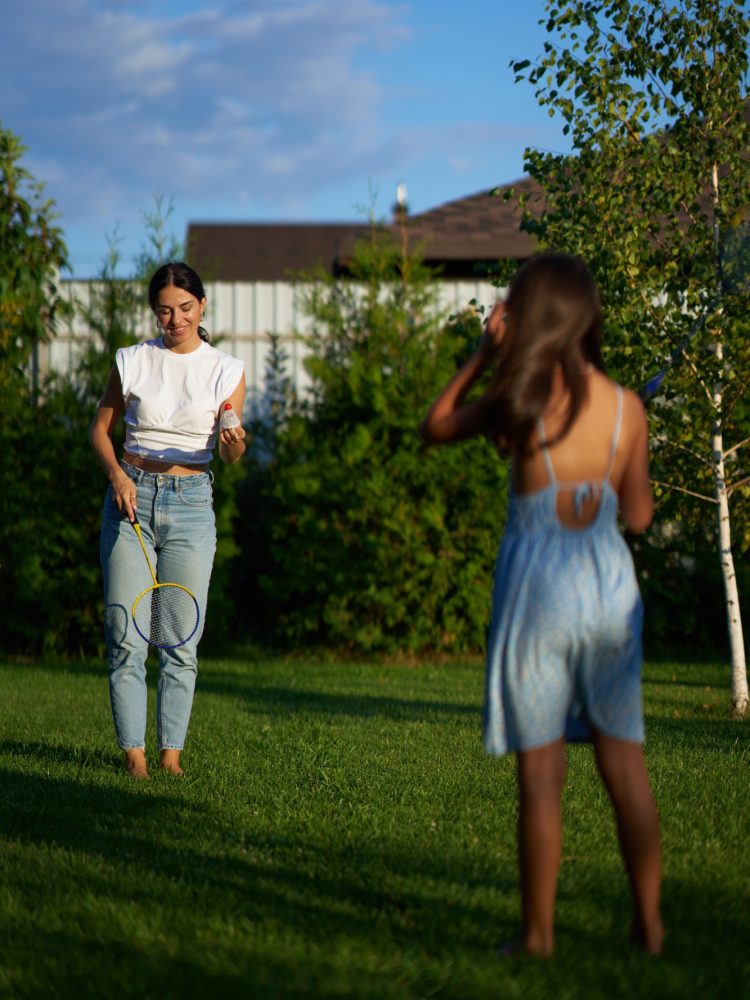 Two people playing badminton in a sunny backyard during late afternoon